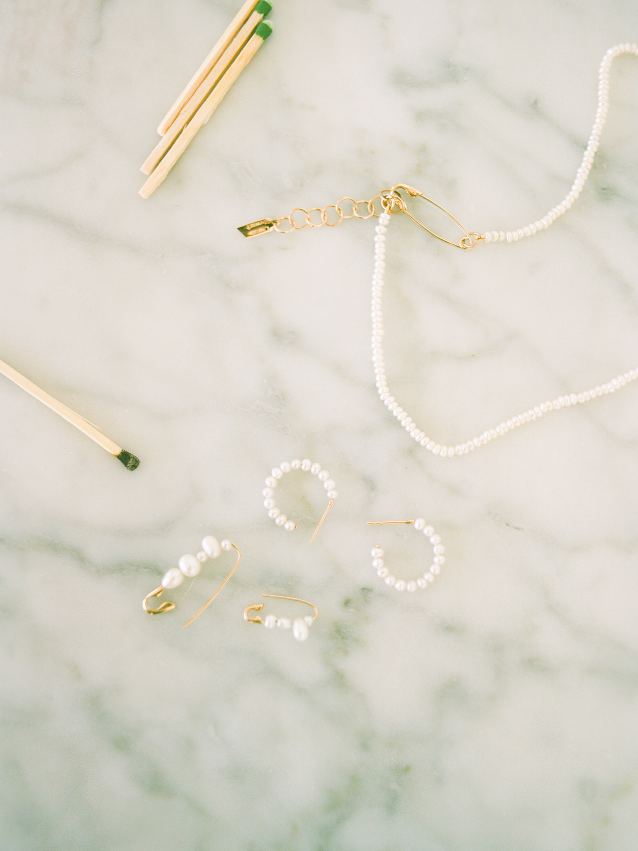 Flat lay of mini mixed pearl safety pin earring on marble backdrop with other pearl styles
