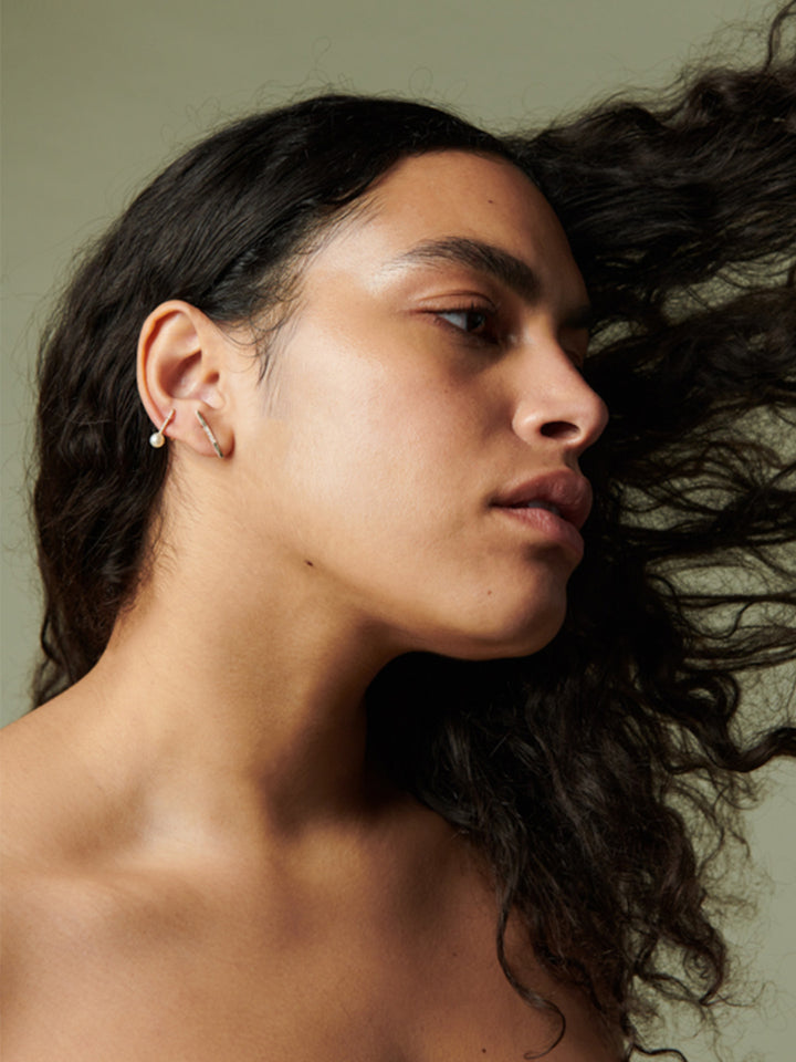 14kt Yellow Gold Diamond Rod Stud Earring pictured on model. Light olive background.