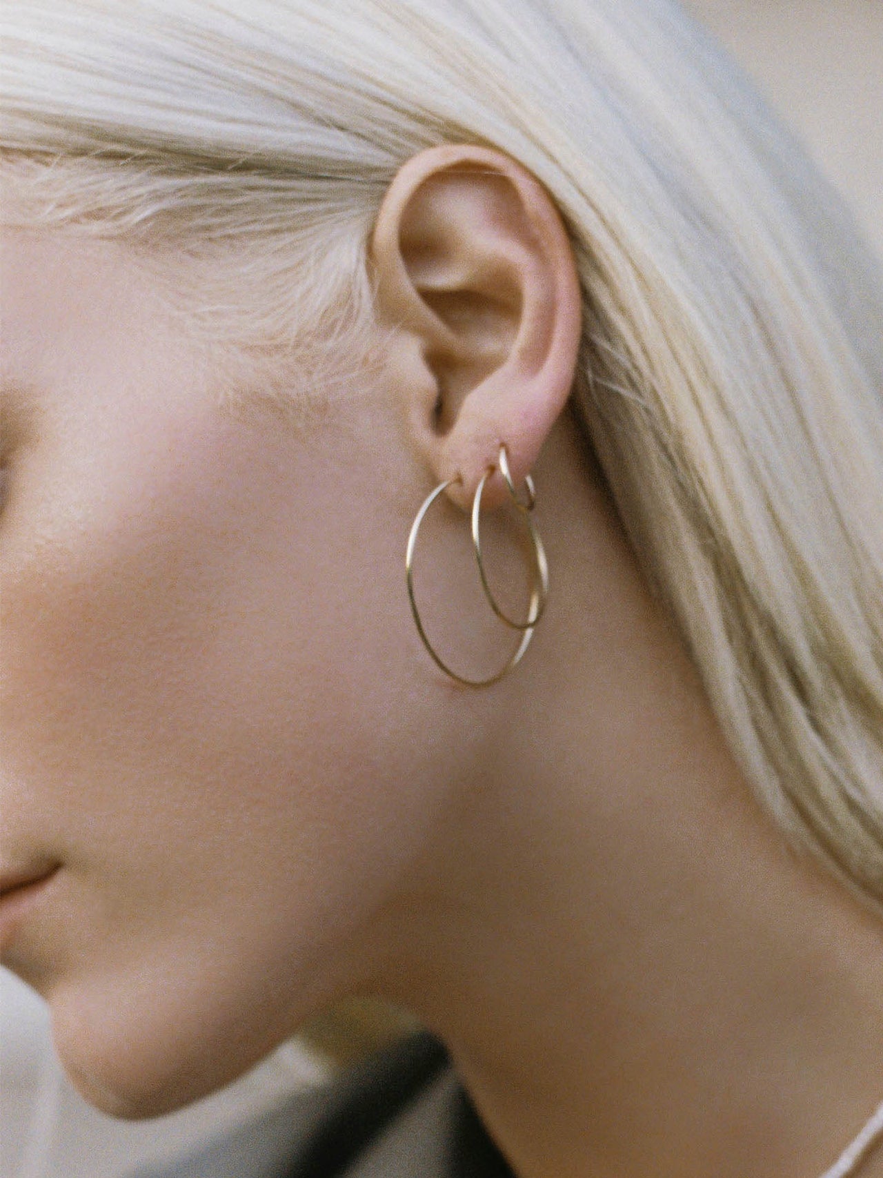 On model close up shot of ear wearing the Valle Hoops (14Kt Yellow Gold Hoops 0.47” Diameter Thickness: 1mm) along with the Nakita Hoops (14Kt Yellow Gold Ultralight Infinity Hoop Earrings  Diameter: 1.4”) 