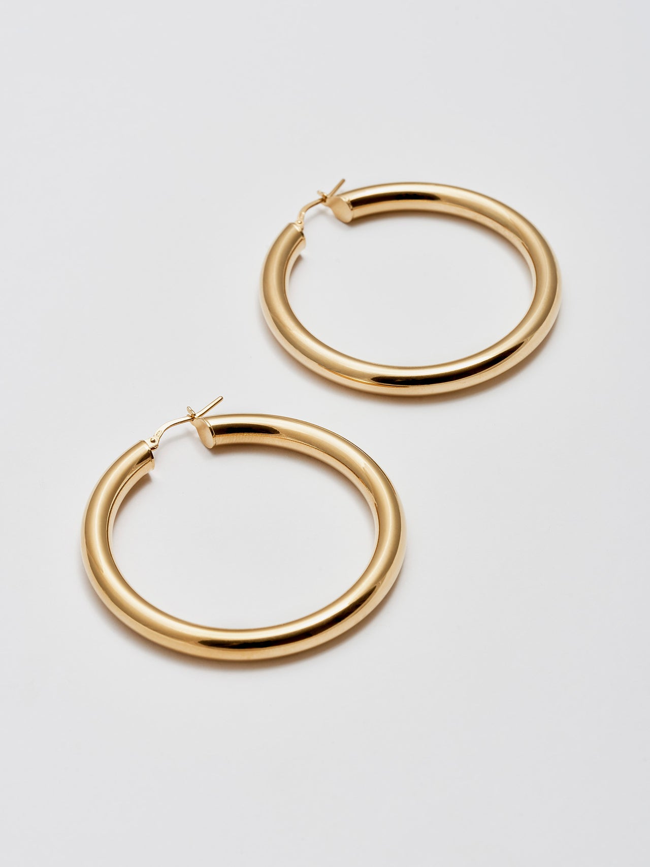 Side angle product Shot of the Tru Hoops in Vermeil gold (Vermeil Hoops 49.5mm diameter 5mm thick) Background: Grey backdrop