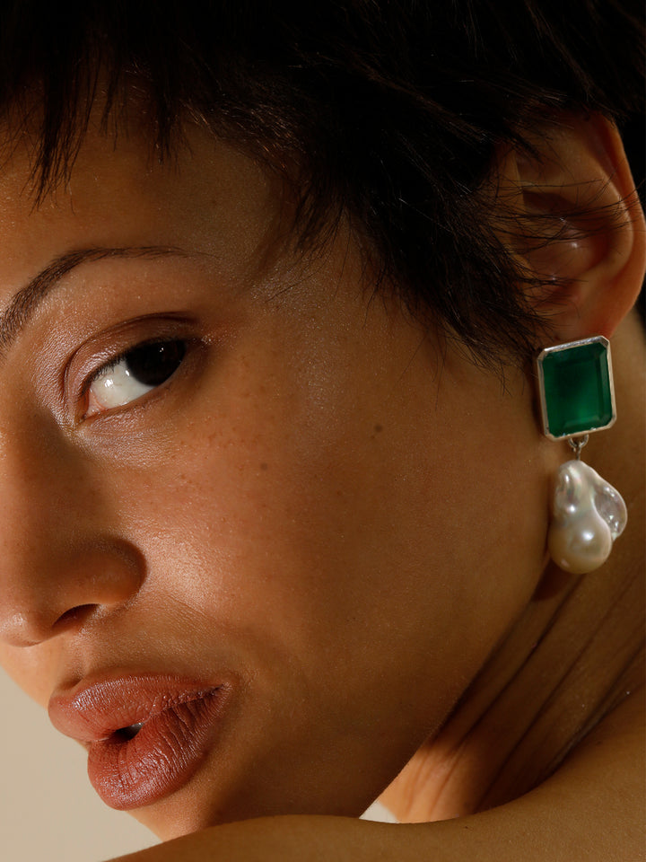 Close up on model shot of the Bronte Earring ( Silver Dangle Earring with a 15×19mm Emerald Cut Green Quartz, Approx 17.1ct Mined in Brazil, Cut in India Approx 25×18mm with a White Baroque Pearl) Background: Grey Backdrop