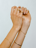 Shot of a model's two hands wearing Mini Heart Signet Ring (14Kt Shiny Yellow Gold Ring with 5mm Mini Heart Face), Gold Plated Herringbone Bracelet,  