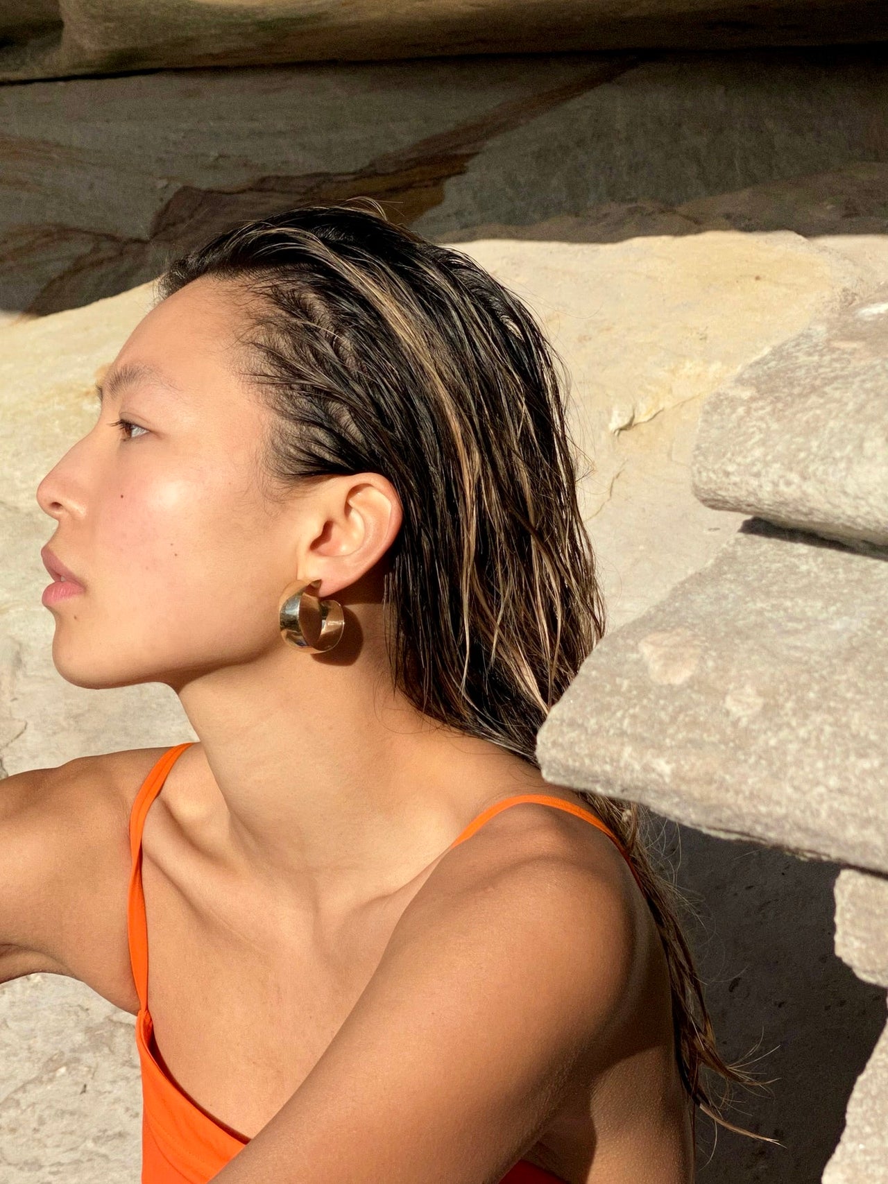 On model side profile shot wearing the Product shot of the XL Dome Hoops(Sterling Silver Hoop Earrings 30mm Diameter 12mm Wide) Background: Rocks and sand