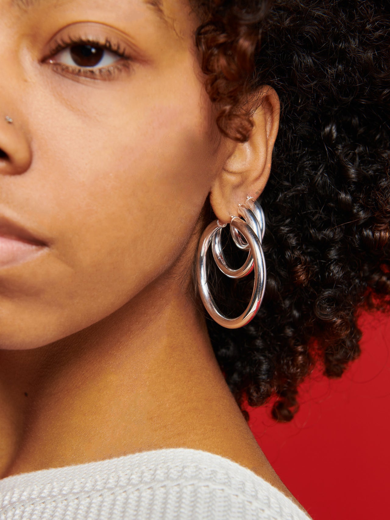 Sterling Silver Large Tru Hoops pictured on model layered with Small and Medium. Red background. 